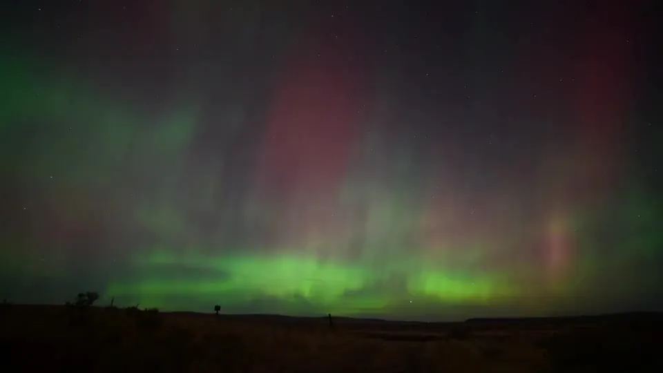 Green and rose aurora curtains above a dark horizon.